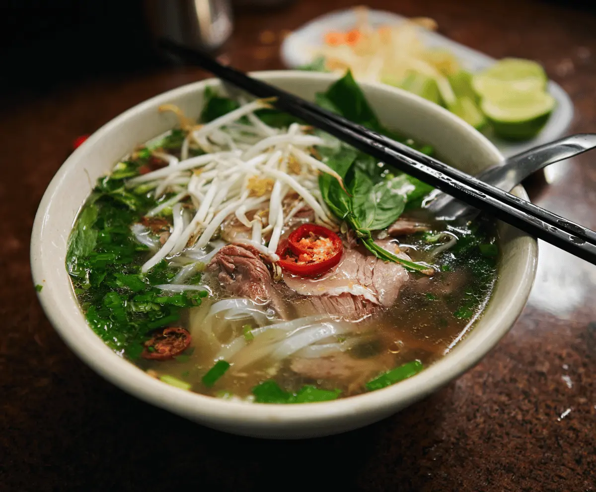 Traditional Vietnamese Pho bowl with rice noodles, sliced beef, fresh herbs, bean sprouts, lime, and chili peppers ready to serve