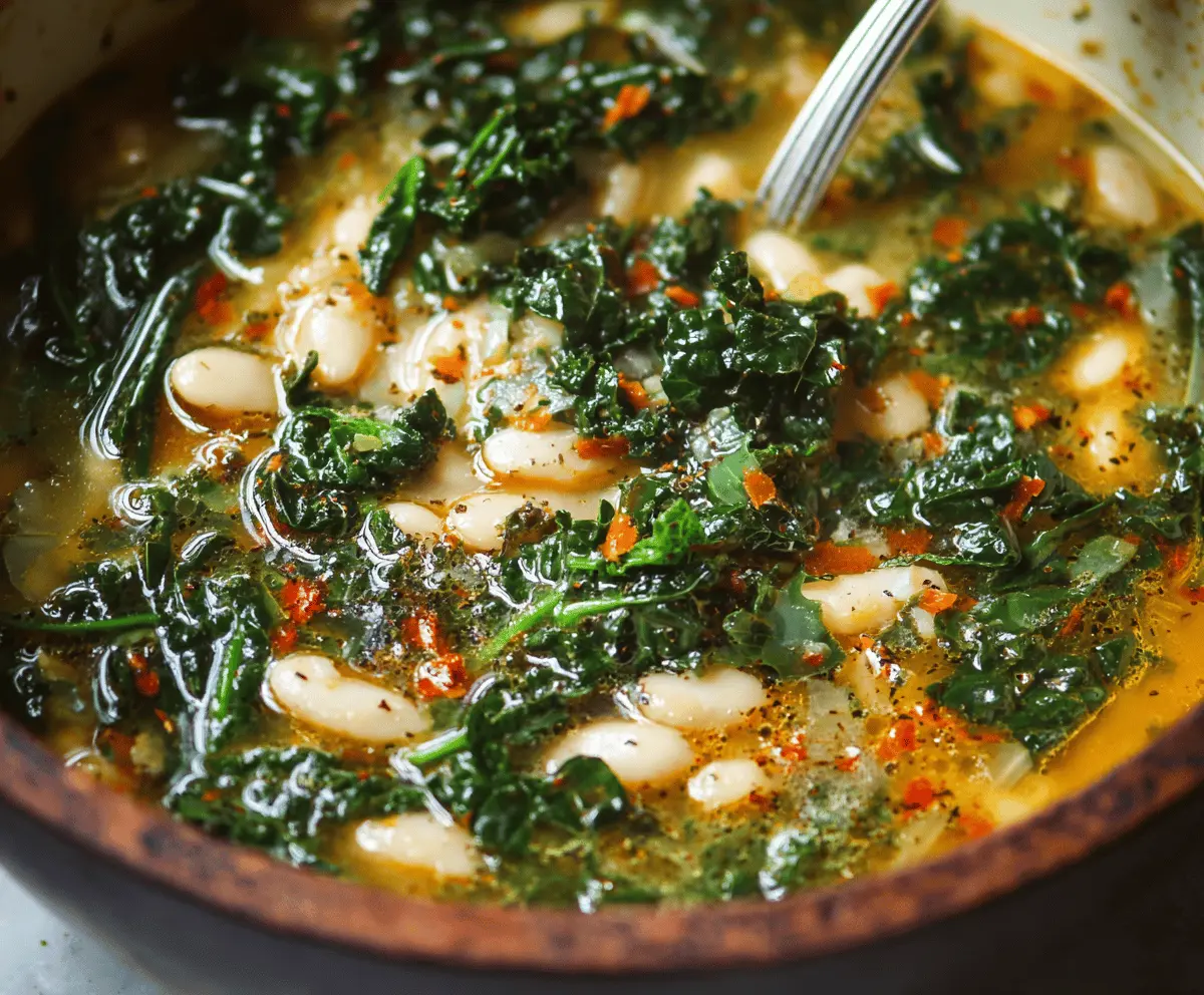 A bowl of hearty white bean and kale soup garnished with herbs, served with fresh bread on the side.