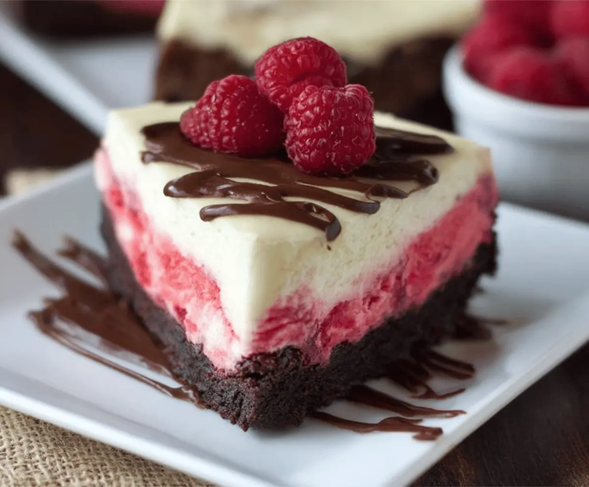 Delicious Raspberry Brownie Cheesecake slice showcasing rich chocolate, fresh raspberries, and creamy cheesecake on a decorative plate
