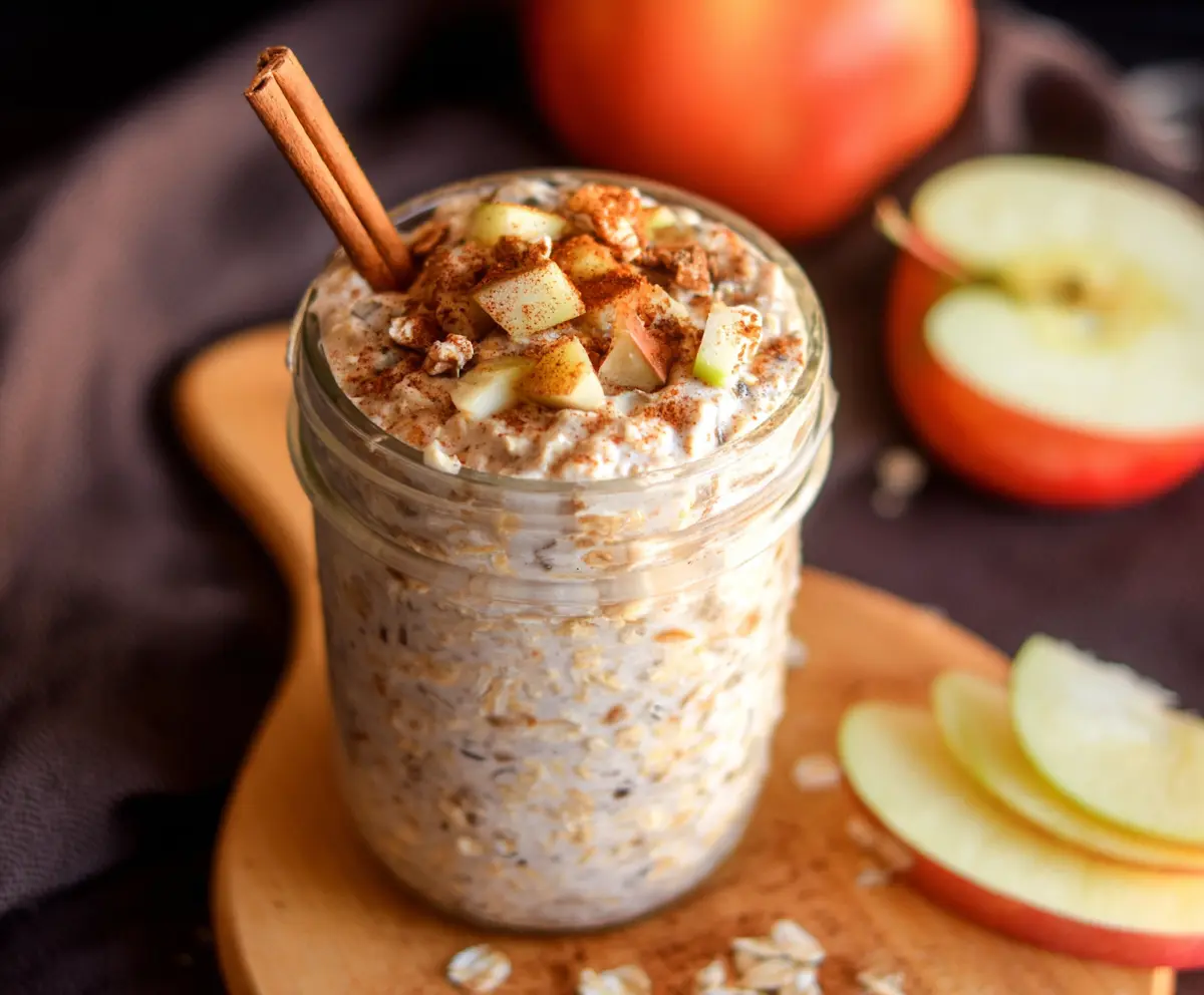 Delicious Apple Cinnamon Protein Overnight Oats in a glass jar, topped with sliced apples and cinnamon for a healthy breakfast.