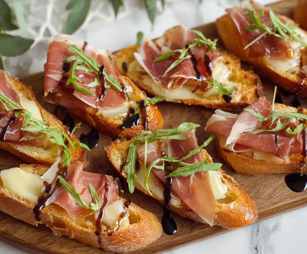 Delicious Brie and Prosciutto Crostini served on a wooden platter, garnished with fresh herbs for an elegant appetizer.