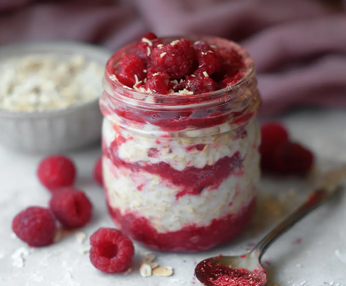 Delicious Raspberry Cheesecake Overnight Oats in a jar topped with fresh raspberries and cream