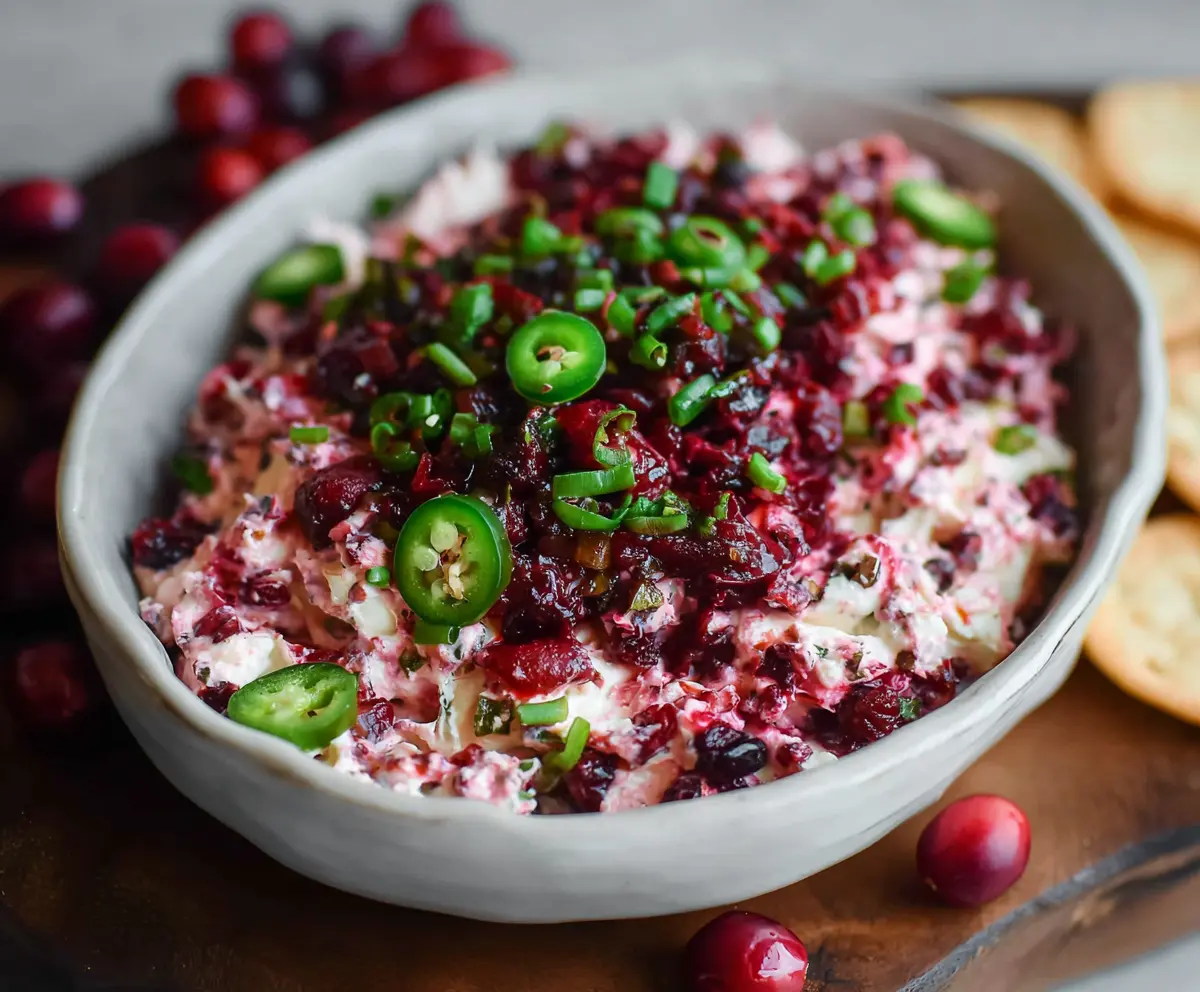 Creamy cranberry jalapeno cream cheese dip garnished with fresh herbs, perfect for holiday parties.